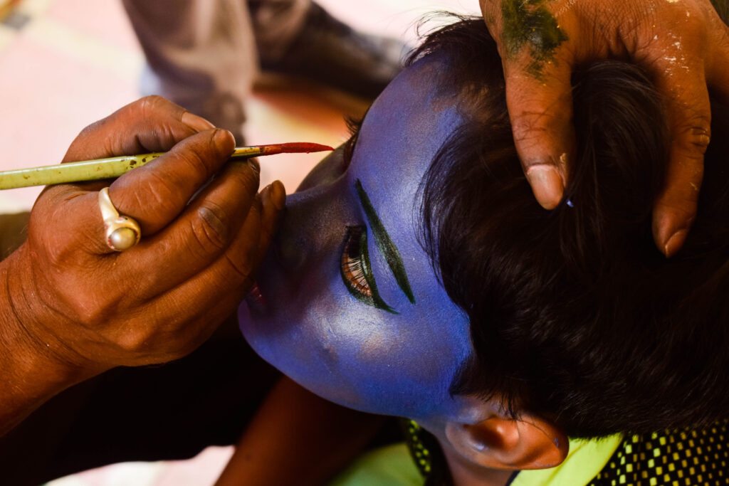 A child getting his face painted as Lord Krishna